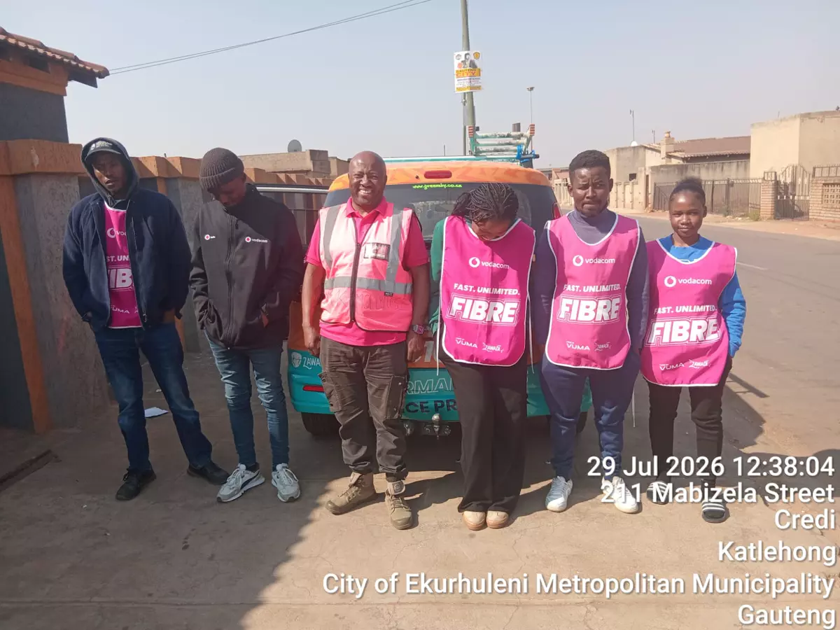 Five people wearing branded pink bibs standing in front of a vehicle