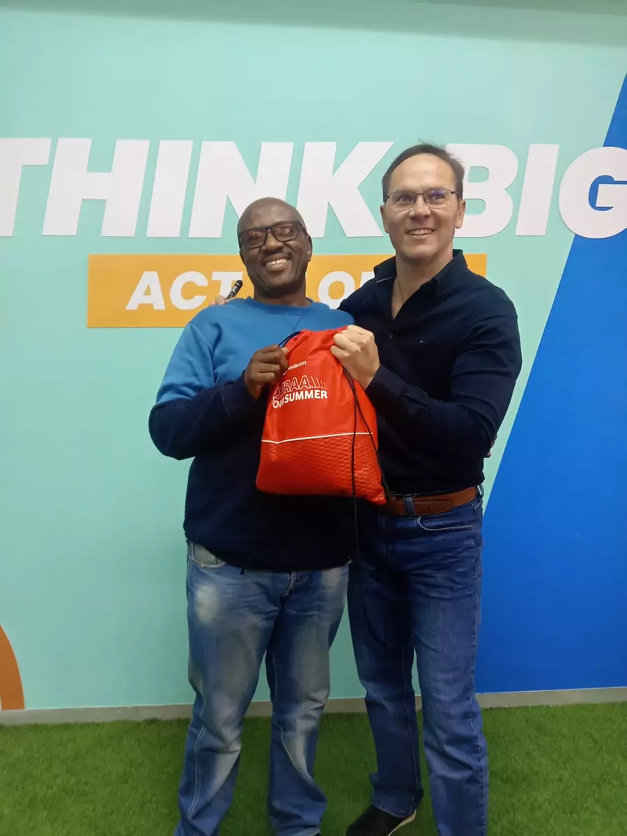 Two men holding a red promotional bag against a branded wall