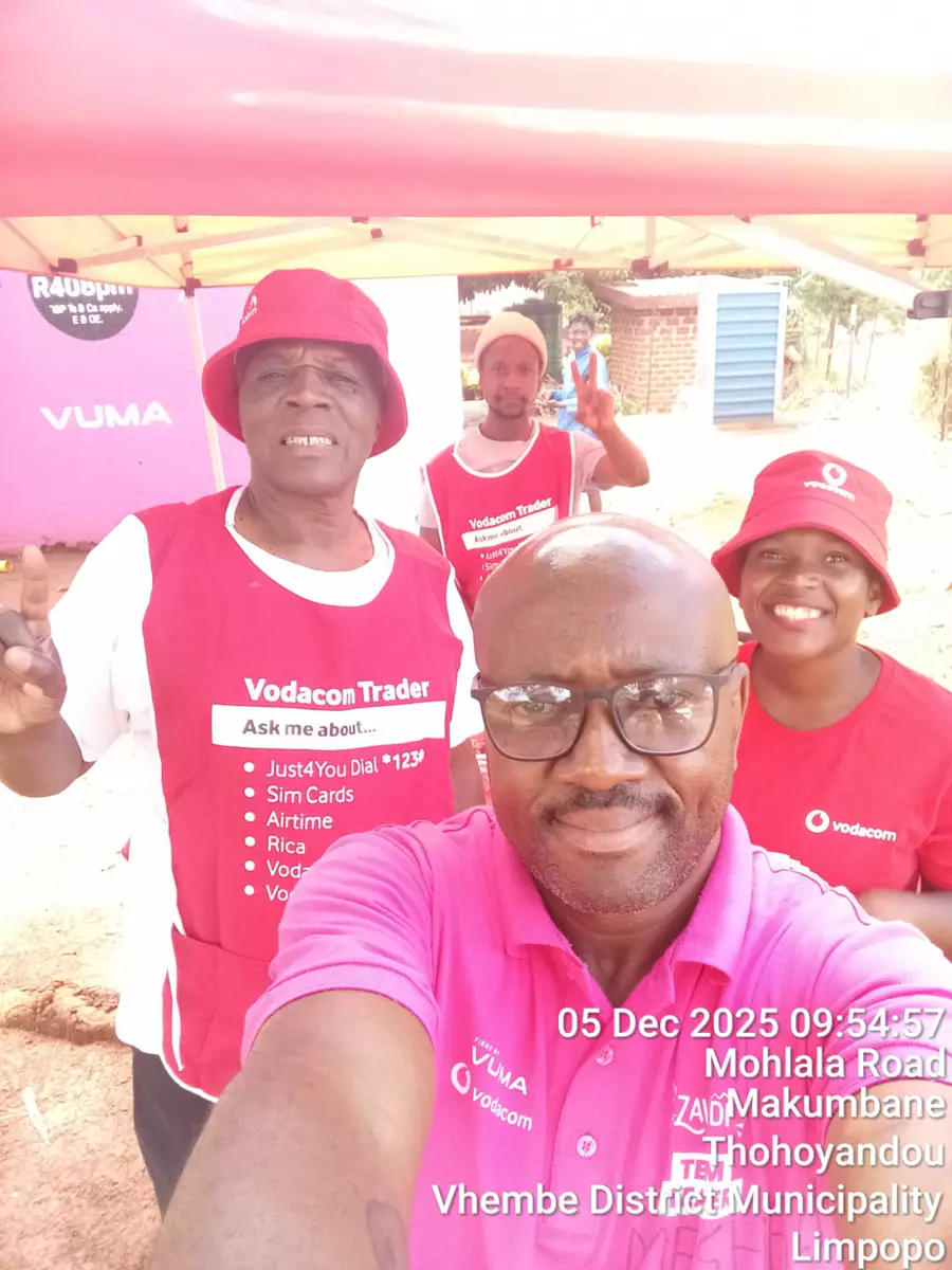 Four people in promotional apparel taking a group selfie under a tent