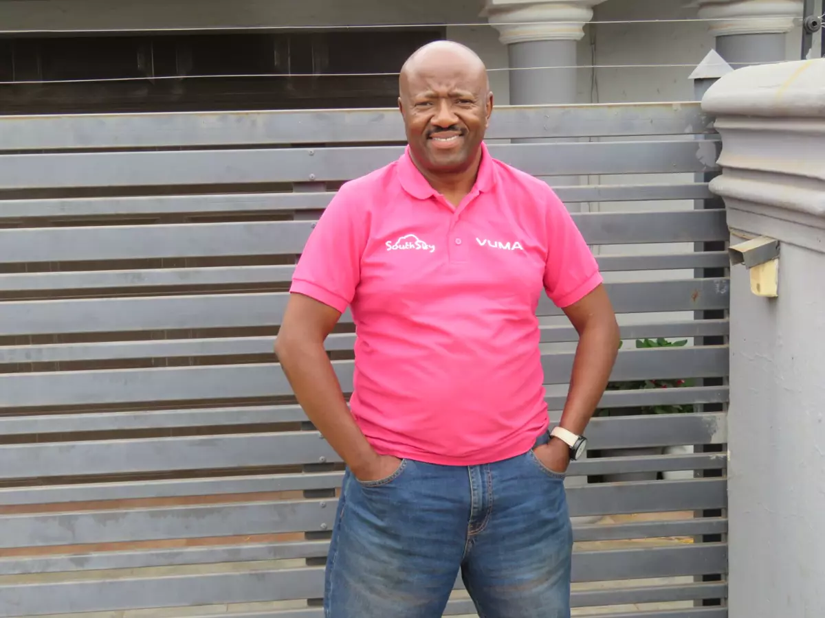 Smiling man in a pink polo shirt standing in front of a grey gate