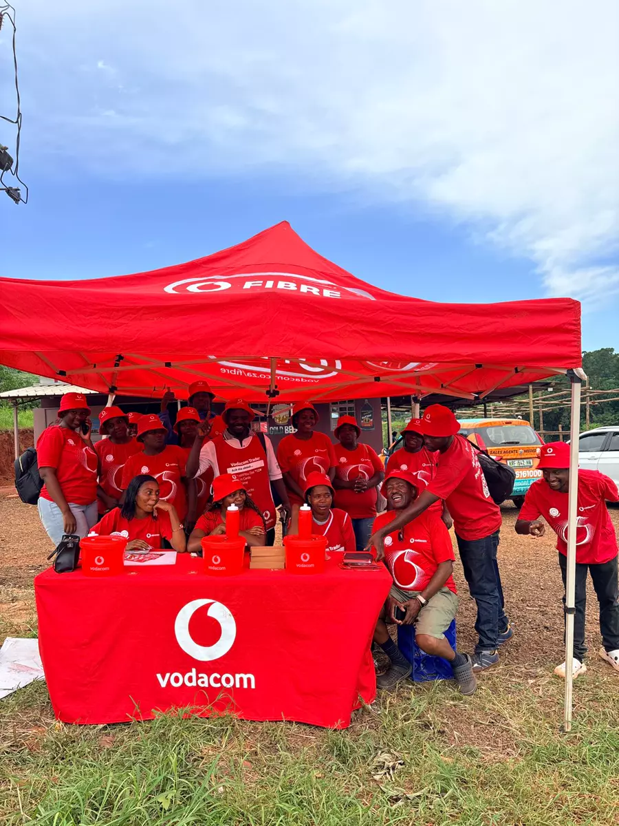 Group in red promotional shirts and hats under a red tent with a branded table