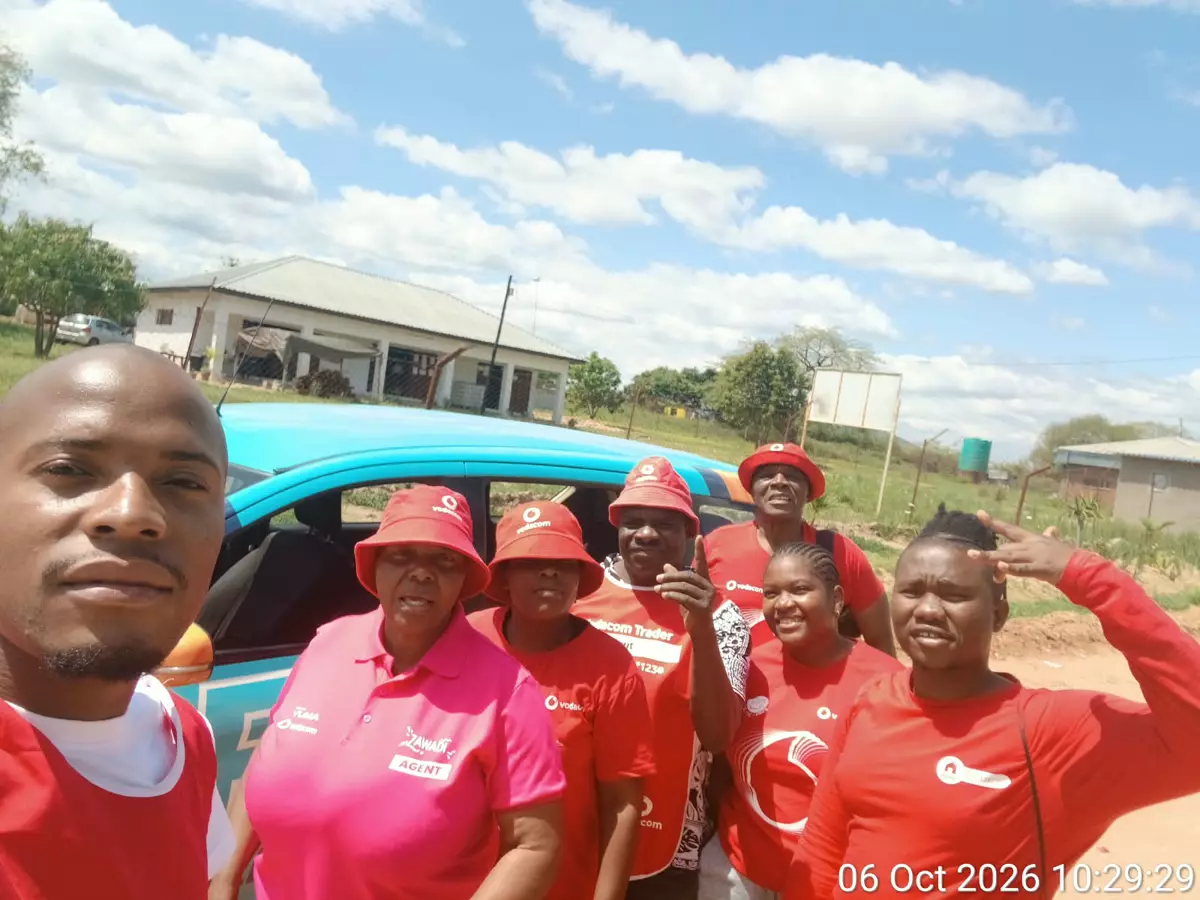 Group of people in red shirts and hats posing outdoors next to a blue car